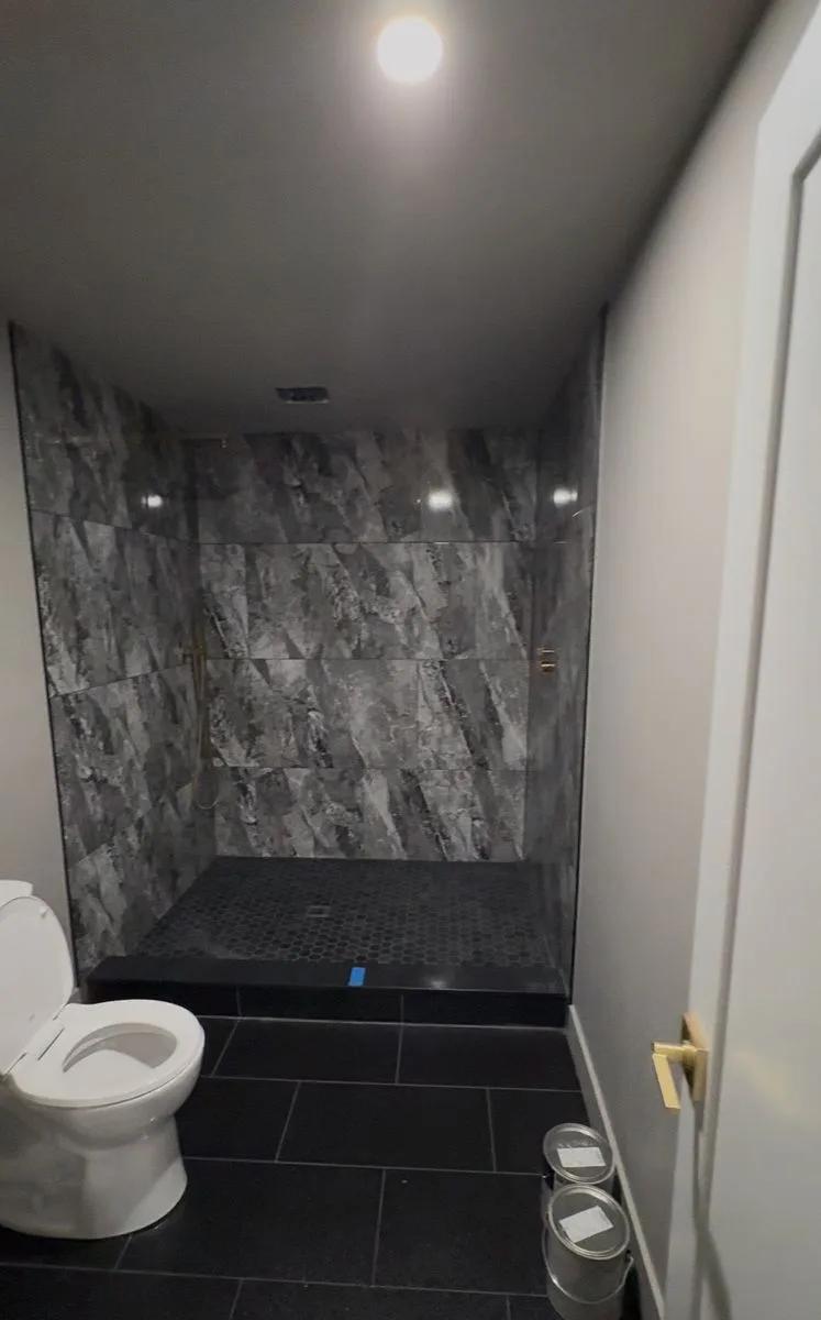 Finished luxury bathroom — full-height marble-look tile, glass shower enclosure, dark slate floor tile