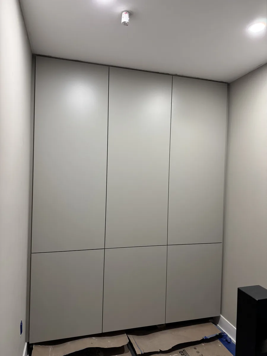 Finished floor-to-ceiling storage wall — grey flush-panel cabinet doors with integrated handles, full-height custom millwork