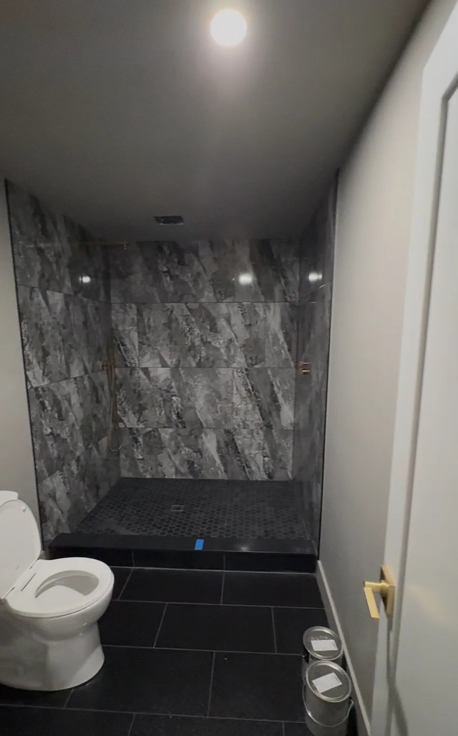 Finished luxury bathroom — full-height marble-look porcelain tile, wall-hung toilet, black hexagon floor tile