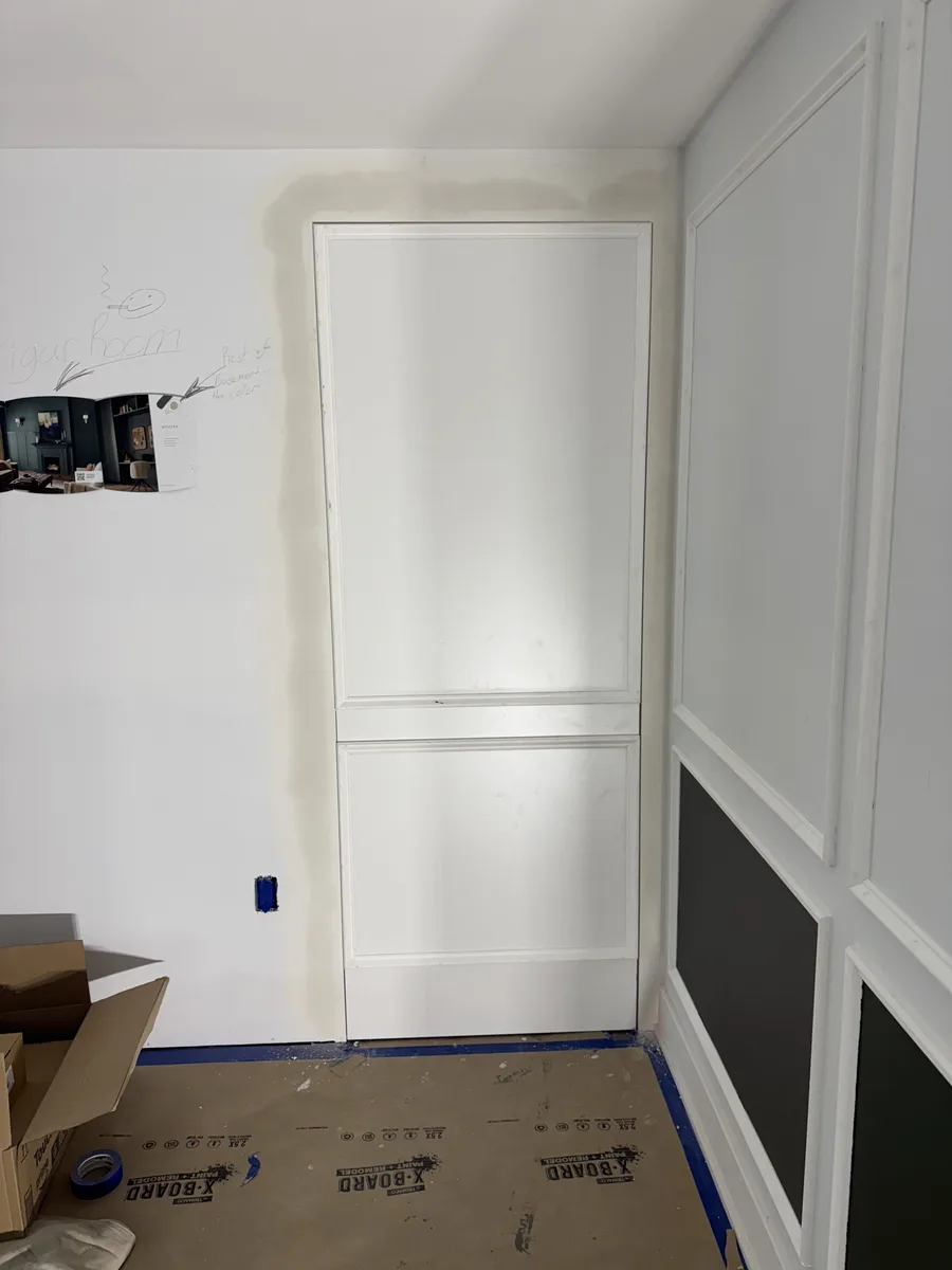 During construction — primed white drywall with design notes and colour swatches pinned to wall, cigar room layout marked out